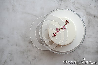 Small ousse cake with smooth white glaze decorated with dried rose buds Stock Photo