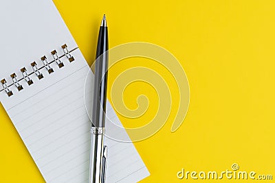 Small paper notepad with blank page, pen on solid yellow backgrond using as meeting note, writing message or task list on working Stock Photo