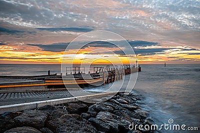 Small pier extending into silky smooth ocean at sunset. Stock Photo