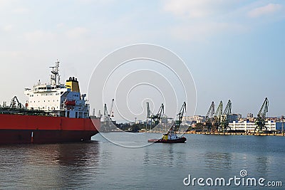 A small pilot ship leads a large red cargo ship at the seaport on a windless autumn day Stock Photo