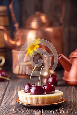 Small portion cheesecake with fresh sweet cherries against of cooper dish and scattered sweet cherries over on old wooden Stock Photo