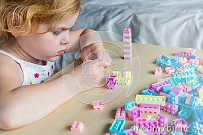 Small preschooler girl playing with colorful toy building blocks, sitting at the table Stock Photo