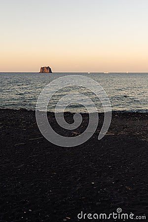 The small promontory of Strombolicchio from Stromboli`s black beach at sunset in Sicily, Italy Stock Photo