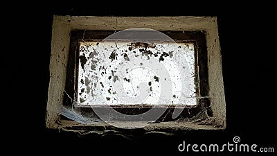 A small rectangular dirty and dusty web window in a large basement. White light penetrates the dark basement Stock Photo