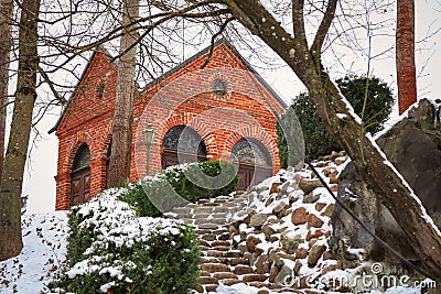 Small red brick old house on hill visible from leading down stairs with hedges covered in snow Stock Photo