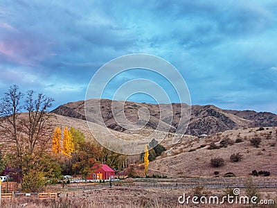 Small red farm shed in the dry brown hills under cloudy autumn sky in New Zealand Stock Photo