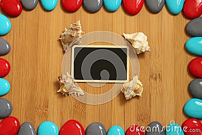 Small red gray and blue pebbles arranged all around a brown bamboo wood floor with in the center an empty slate to write a message Stock Photo
