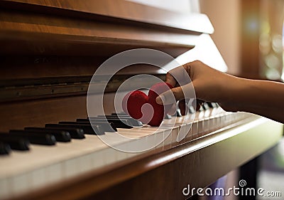 The small red heart was put on piano keys by human hand,warm light tone,reflection of sunlight is shining to piano Stock Photo