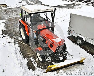 Small red tractor with snow plow for street cleaning in winter season Editorial Stock Photo