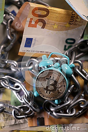 Small retro alarm clock with bitcoin gold coin and euro banknotes in a background. New financial asset. Stock Photo