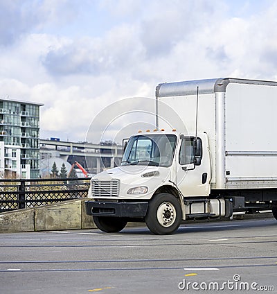 Small rig semi truck with box trailer for local deliveries driving on the bridge on the city street Stock Photo