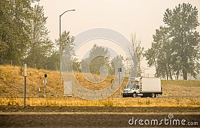 Small rig semi truck with refrigerated box trailer transporting cargo running on the road in smoke and smog from a forest fire Stock Photo