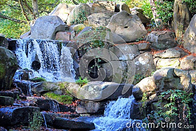 Small rocky waterfall in a woodland glade with sunlight streaming through Stock Photo