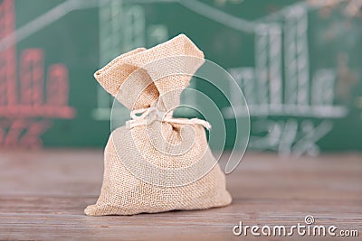 A small sack full of coins in front of a small blackboard with financial graphics Stock Photo