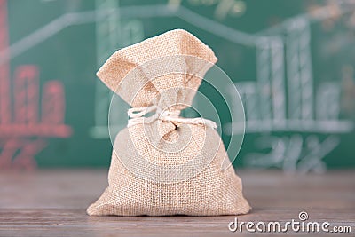 A small sack full of coins in front of a small blackboard with financial graphics Stock Photo