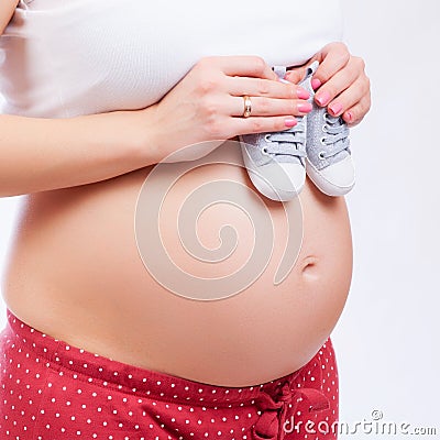 Small shoes for the unborn baby in the belly of pregnant woman Stock Photo