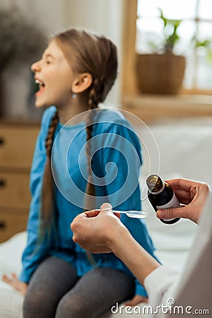 Small sick mischievous girl loudly refusing to take throat syrup Stock Photo