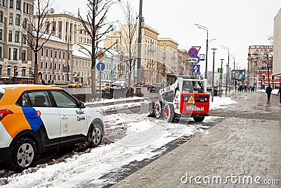 A small snowplow tractor removes snow drift from the street. Editorial Stock Photo