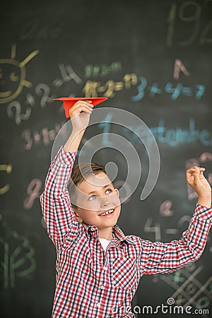 A small student launches a red airplane in the classroom against the background of a board Stock Photo