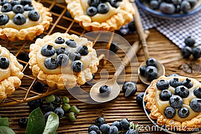 Small tarts made of puff pastry with addition fresh blueberries and caramel chocolate custard on a wooden rustic table, close up. Stock Photo