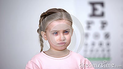Small tearful girl looking into camera, afraid to wear glasses vision correction Stock Photo