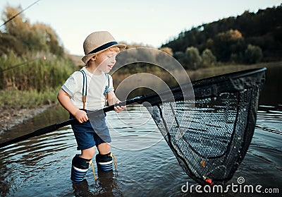 A small toddler boy standing in water and holding a net by a lake, fishing. Stock Photo