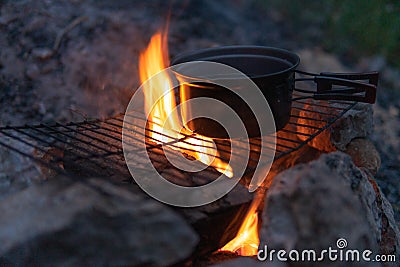 Small tourist pot, a bowl of water. Cooking in the field. Fire, Camping. Leisure and hobbies. Night, Dinner. Place for text Stock Photo