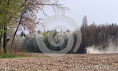 A small tractor cultivates a plowed field in the forest. Stock Photo