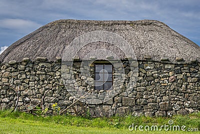 A small traditional stone built cottage with a thatched roof. a collection of metal rims for cart wheels Stock Photo