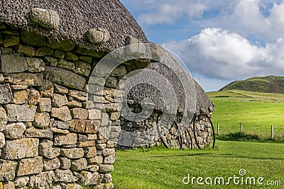 A small traditional stone built cottage with a thatched roof. a collection of metal rims for cart wheels Stock Photo