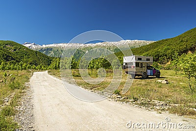 Small travel vehicle camping van is parked under huge mountain formation. Tourism vacation and travel. Camper van and Stock Photo