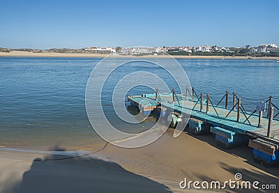 Small turquoise wooden pier at Praia das Furnas sand beach with view over the Mira river to Vila Nova de Milfontes Stock Photo