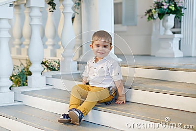 Small very cute, charming boy in yellow trousers sits on the sta Stock Photo