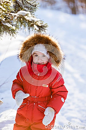 Small very cute girl in a red suit with fur hood costs about trees in winter forest background Stock Photo