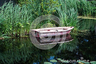 Small vessel reflecting in a creek with green water reeds, Barendrecht, The Netherlands Stock Photo
