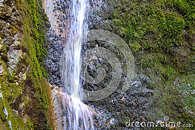 Small waterfall on a rocky stream stone background. Mountain covered with green moss. Concept for refreshing coolness or Stock Photo