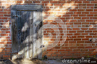 A small weathered wooden door in an old brick wall in dappled sunlight Stock Photo