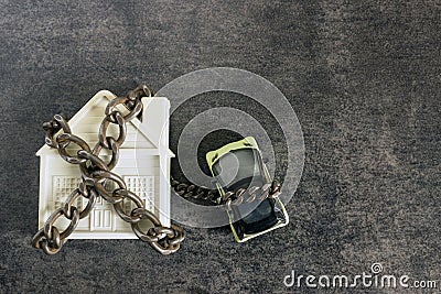 Small white house, car and a decorative chain on a dark background. Concept - risks, lose property, seize, mortgage. Stock Photo