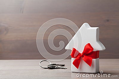 Small white house decorated red bow ribbon with bunch of keys on wooden background. Gift, real estate or buying a new home Stock Photo