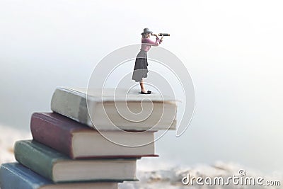 Miniature woman looks at the infinity with the spyglass on a scale of books Stock Photo