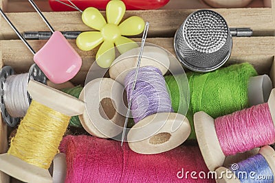 A small wooden box with colored threads on spools of green, blue, pink, a sewing needle and sewing bobbins Stock Photo