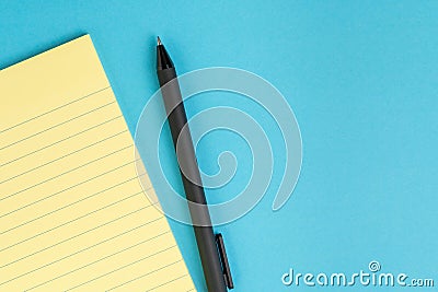 Small yellow paper notepad with blank page, pen on solid blue background using as meeting note, writing message or task list on Stock Photo