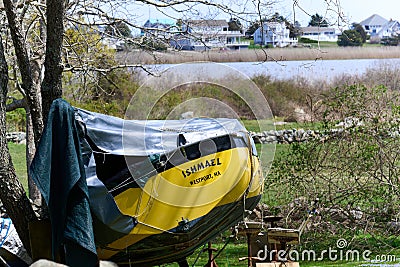 A small yellow sailboat is covered by a tarp for winter storage Editorial Stock Photo