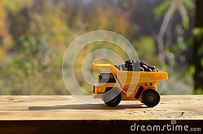 A small yellow toy truck is loaded with brown coffee beans. A car on a wooden surface against a background of autumn forest. Extr Stock Photo