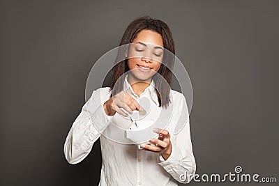 Smart black woman putting in piggy bank one coin on gray background Stock Photo