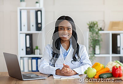 Smart eating and healthy nutrition. Portrait of positive black dietitian looking at camera and smiling at workplace Stock Photo