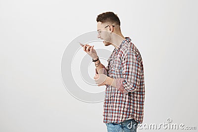 Smart guy talks with his phone assistant. Portrait of handsome young man in glasses standing in profile while holding Stock Photo