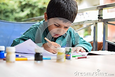 Smart Indian little boy perform thumb painting with different colourful water colour kit during the summer vacations, Cute Indian Stock Photo