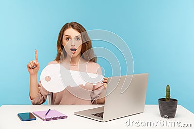Smart inspired woman employee sitting at workplace holding big key and pointing finger up with genius idea Stock Photo