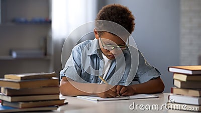 Smart little boy neatly writing homework in his notebook, diligent schoolboy Stock Photo